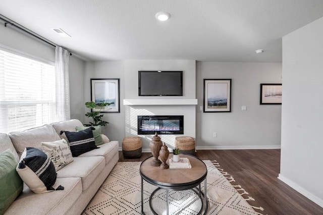 living room featuring a glass covered fireplace, visible vents, baseboards, and wood finished floors