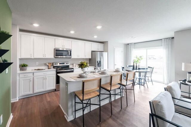 kitchen with dark wood finished floors, appliances with stainless steel finishes, a breakfast bar area, white cabinets, and light countertops