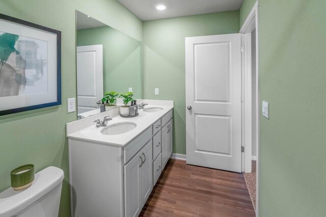 bathroom with double vanity, toilet, wood finished floors, and a sink