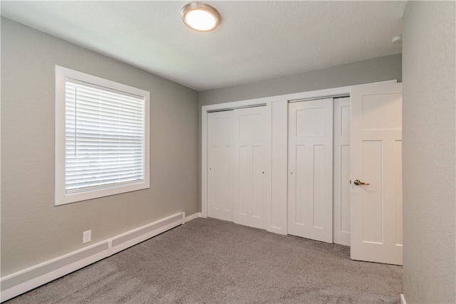 unfurnished bedroom with carpet flooring, a baseboard radiator, and two closets