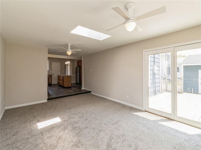 unfurnished living room featuring ceiling fan with notable chandelier, carpet floors, and a skylight