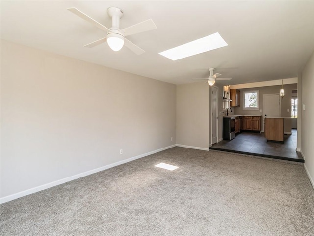 unfurnished living room with a skylight, ceiling fan, and dark carpet