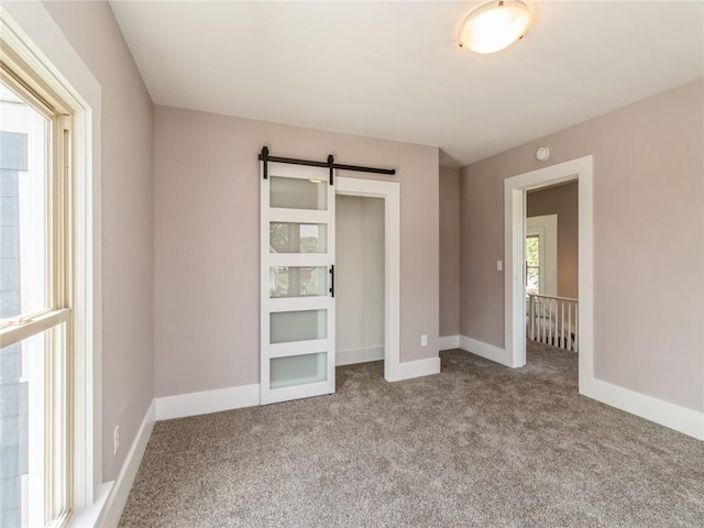 unfurnished bedroom featuring a barn door and light carpet