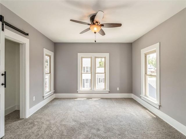 unfurnished room with carpet flooring, a barn door, ceiling fan, and plenty of natural light