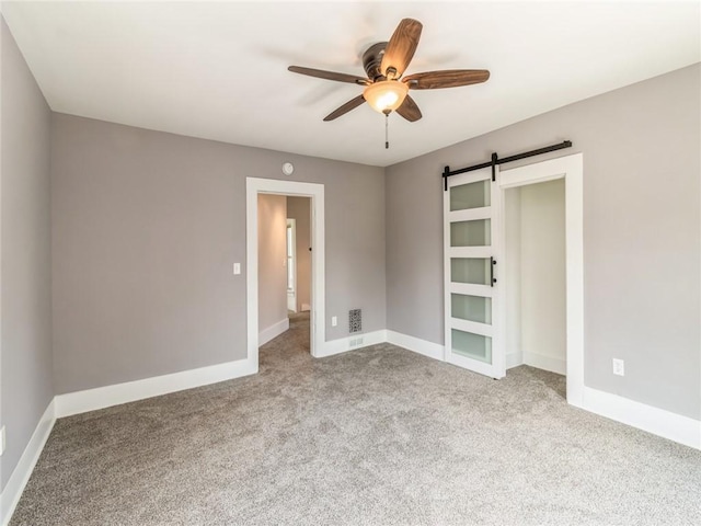 unfurnished bedroom featuring a barn door, ceiling fan, and light colored carpet