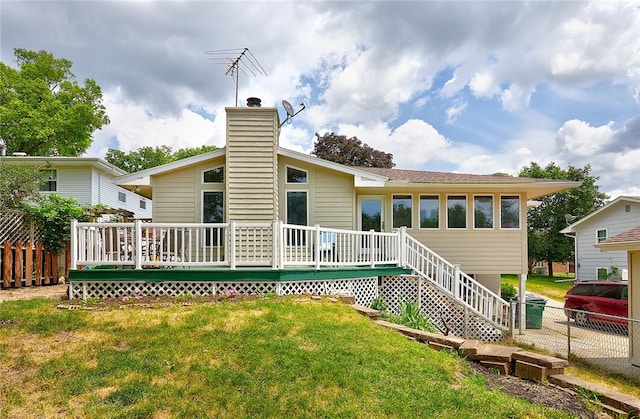 rear view of property with fence, a wooden deck, and a lawn