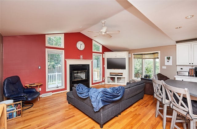 living room with lofted ceiling, ceiling fan, a tiled fireplace, and light wood-type flooring