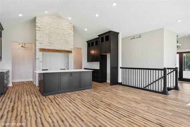 kitchen with light hardwood / wood-style floors, an island with sink, brick wall, high vaulted ceiling, and sink