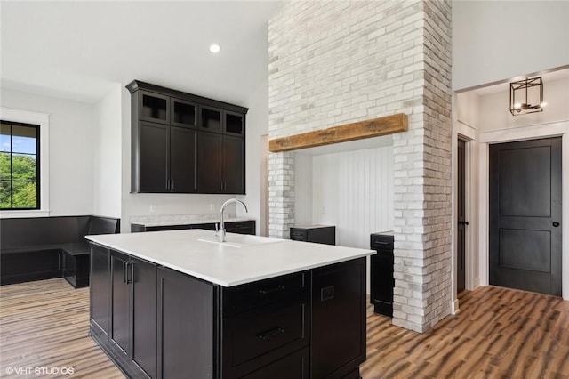 kitchen featuring light hardwood / wood-style floors, hanging light fixtures, brick wall, a kitchen island with sink, and sink