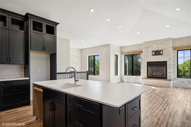 kitchen featuring a large fireplace, light hardwood / wood-style floors, a kitchen island with sink, sink, and lofted ceiling