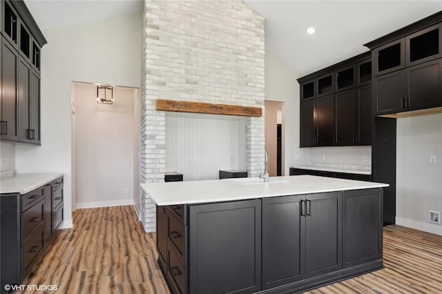 kitchen with light hardwood / wood-style floors, brick wall, a center island with sink, high vaulted ceiling, and sink