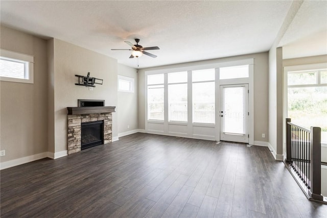 unfurnished living room featuring a fireplace, a wealth of natural light, ceiling fan, and dark wood-type flooring