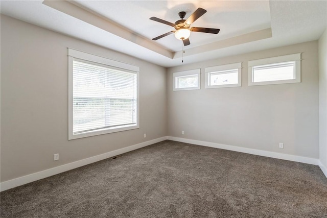 unfurnished room with dark colored carpet, ceiling fan, and a raised ceiling