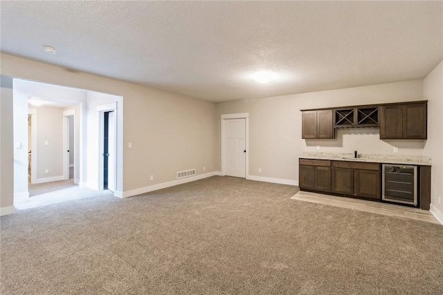 unfurnished living room with indoor wet bar, light colored carpet, a textured ceiling, and wine cooler