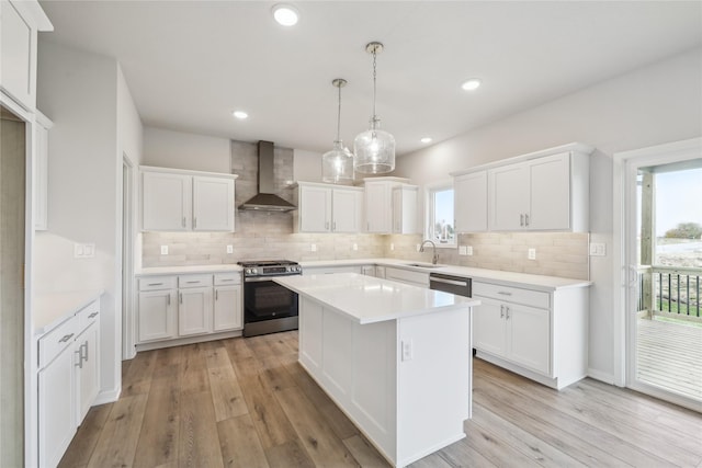 kitchen with wall chimney range hood, stainless steel range with gas stovetop, light hardwood / wood-style floors, white cabinets, and a kitchen island