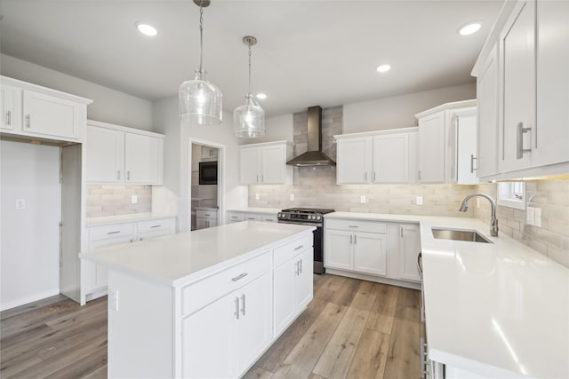 kitchen with sink, white cabinets, a center island, stainless steel gas range oven, and wall chimney range hood