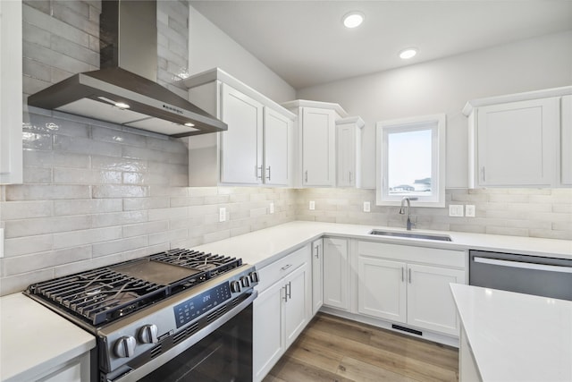 kitchen featuring stainless steel appliances, sink, wall chimney range hood, and white cabinets