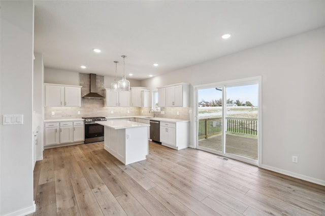 kitchen with pendant lighting, appliances with stainless steel finishes, a center island, white cabinets, and wall chimney exhaust hood