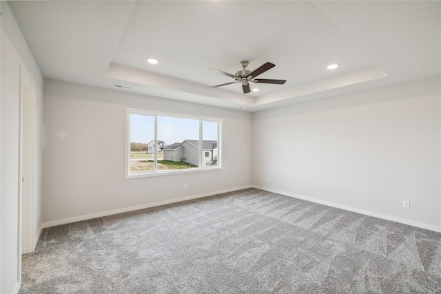 carpeted spare room featuring ceiling fan and a raised ceiling