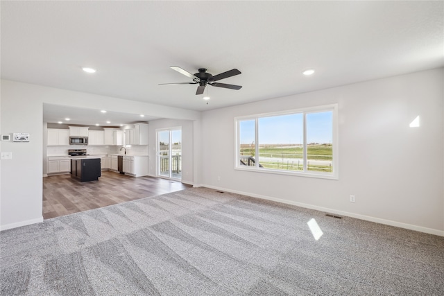 unfurnished living room featuring light colored carpet, sink, and ceiling fan