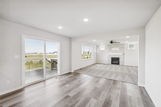 unfurnished living room with ceiling fan, a stone fireplace, and light hardwood / wood-style flooring