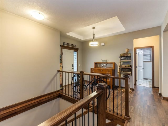 corridor with a tray ceiling, hardwood / wood-style floors, and a textured ceiling