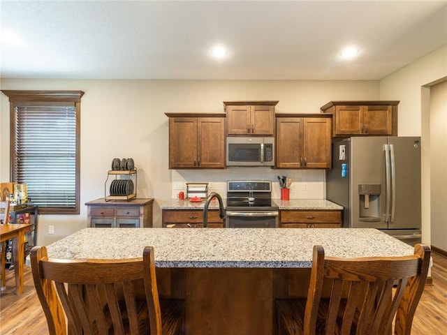 kitchen with stainless steel appliances, light stone counters, light wood-type flooring, and decorative backsplash