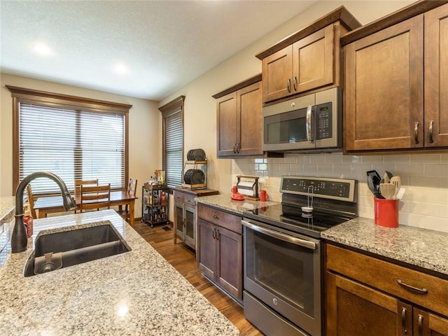 kitchen with sink, stainless steel appliances, dark hardwood / wood-style floors, light stone counters, and tasteful backsplash