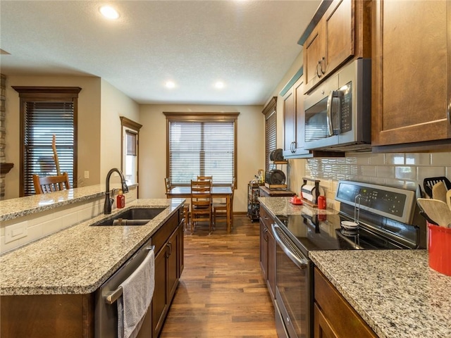 kitchen with tasteful backsplash, sink, dark hardwood / wood-style flooring, stainless steel appliances, and light stone countertops