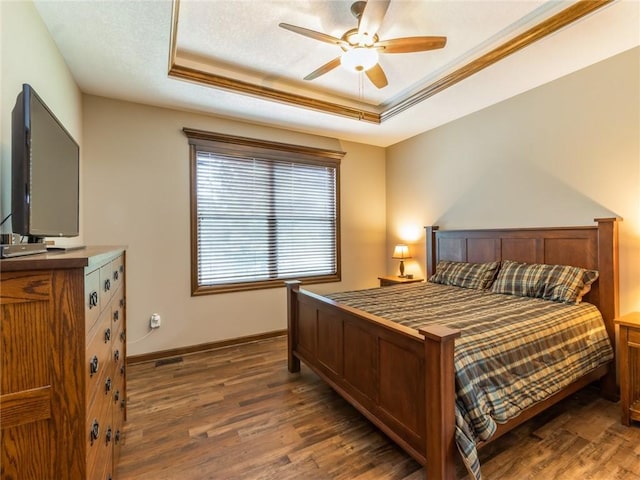 bedroom with dark hardwood / wood-style flooring, a tray ceiling, and ceiling fan