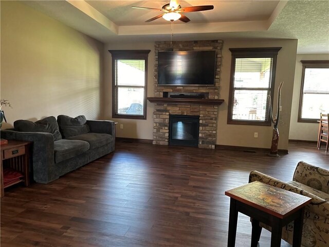 living room featuring dark hardwood / wood-style flooring, a tray ceiling, a fireplace, and a textured ceiling