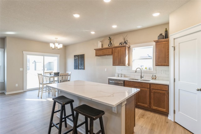 kitchen with sink, decorative backsplash, hanging light fixtures, a center island, and light hardwood / wood-style flooring