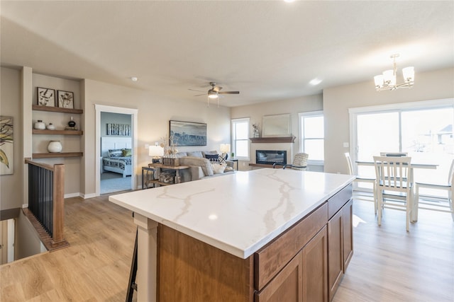 kitchen featuring light stone counters, a center island, hanging light fixtures, light wood-type flooring, and ceiling fan with notable chandelier