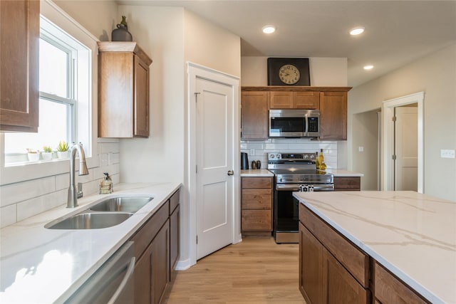 kitchen with appliances with stainless steel finishes, sink, decorative backsplash, plenty of natural light, and light wood-type flooring