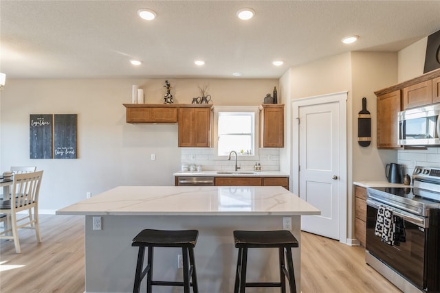 kitchen featuring sink, a center island, stainless steel appliances, light hardwood / wood-style floors, and decorative backsplash