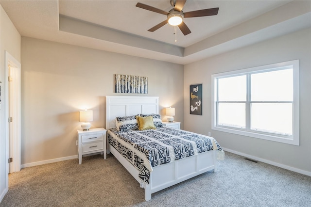 carpeted bedroom featuring ceiling fan and a raised ceiling