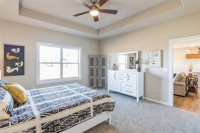 carpeted bedroom with a raised ceiling and ceiling fan