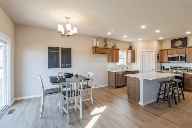 kitchen with a center island, hanging light fixtures, light hardwood / wood-style flooring, appliances with stainless steel finishes, and decorative backsplash