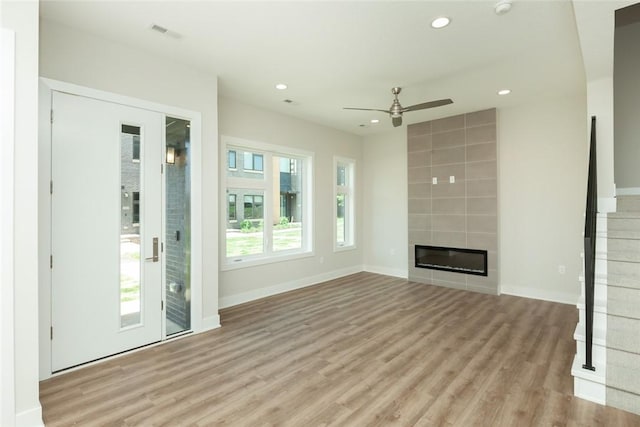 unfurnished living room with ceiling fan, light wood-type flooring, plenty of natural light, and a tiled fireplace