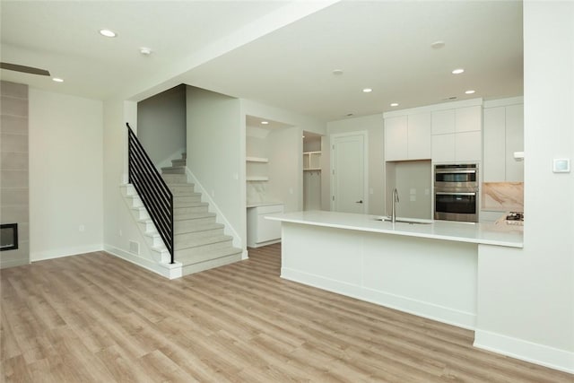 kitchen with a fireplace, double oven, sink, light hardwood / wood-style flooring, and white cabinets