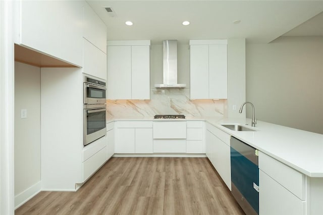 kitchen with sink, stainless steel appliances, wall chimney range hood, backsplash, and white cabinets