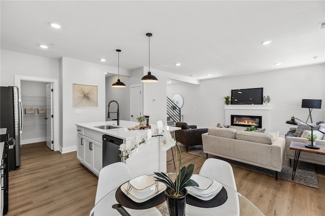 kitchen featuring sink, light hardwood / wood-style floors, pendant lighting, white cabinets, and appliances with stainless steel finishes