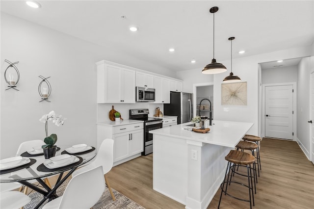 kitchen with stainless steel appliances, a kitchen island with sink, sink, white cabinets, and hanging light fixtures