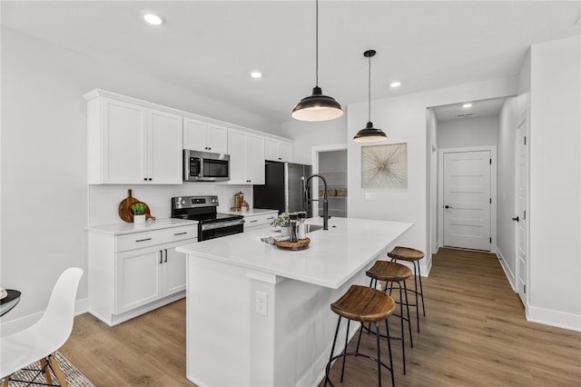 kitchen with white cabinetry, stainless steel appliances, an island with sink, decorative light fixtures, and a kitchen bar