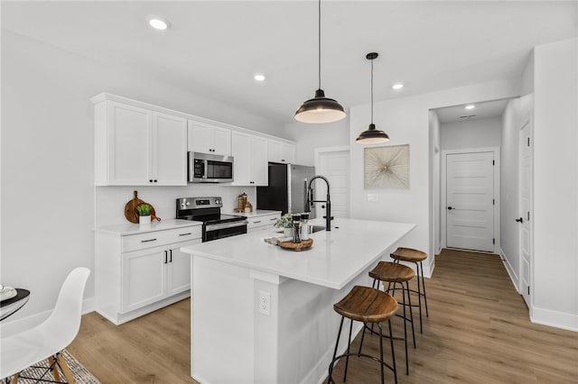 kitchen with hanging light fixtures, white cabinetry, an island with sink, and appliances with stainless steel finishes