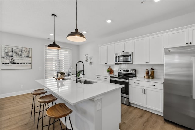 kitchen with white cabinetry, sink, stainless steel appliances, pendant lighting, and a center island with sink