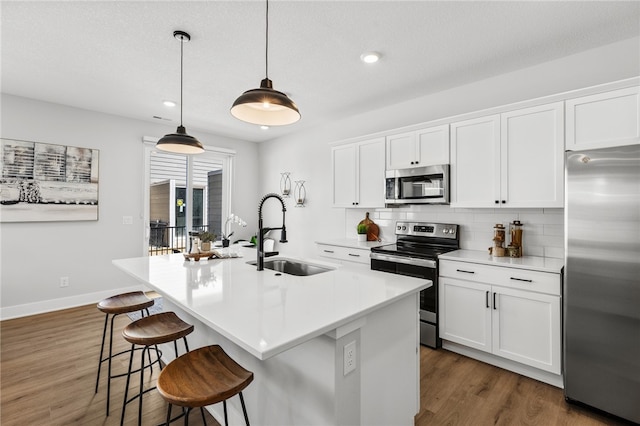 kitchen featuring sink, hanging light fixtures, a kitchen island with sink, white cabinets, and appliances with stainless steel finishes