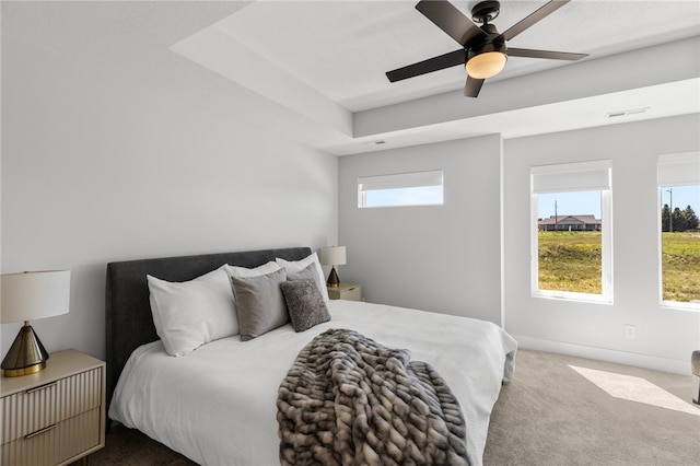 bedroom with carpet, ceiling fan, a tray ceiling, and multiple windows