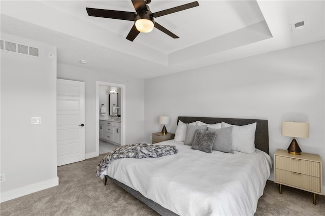 carpeted bedroom featuring a raised ceiling, ceiling fan, and ensuite bathroom