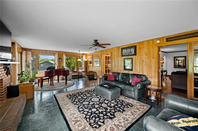 living area featuring stone finish floor, a fireplace, wood walls, and ceiling fan